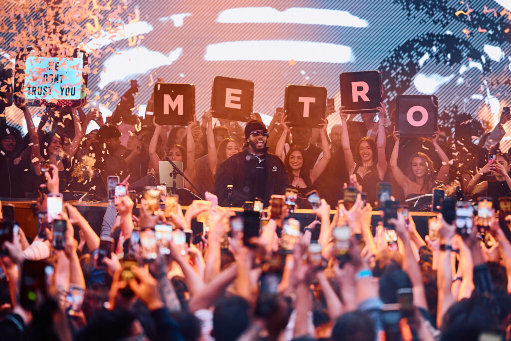 Shot from the crowd, Metro Boomin is behind the DJ booth with confetti falling, a presentation behind him spelling out "METRO", and a sign to the left that says "WE DON'T TRUST YOU". 