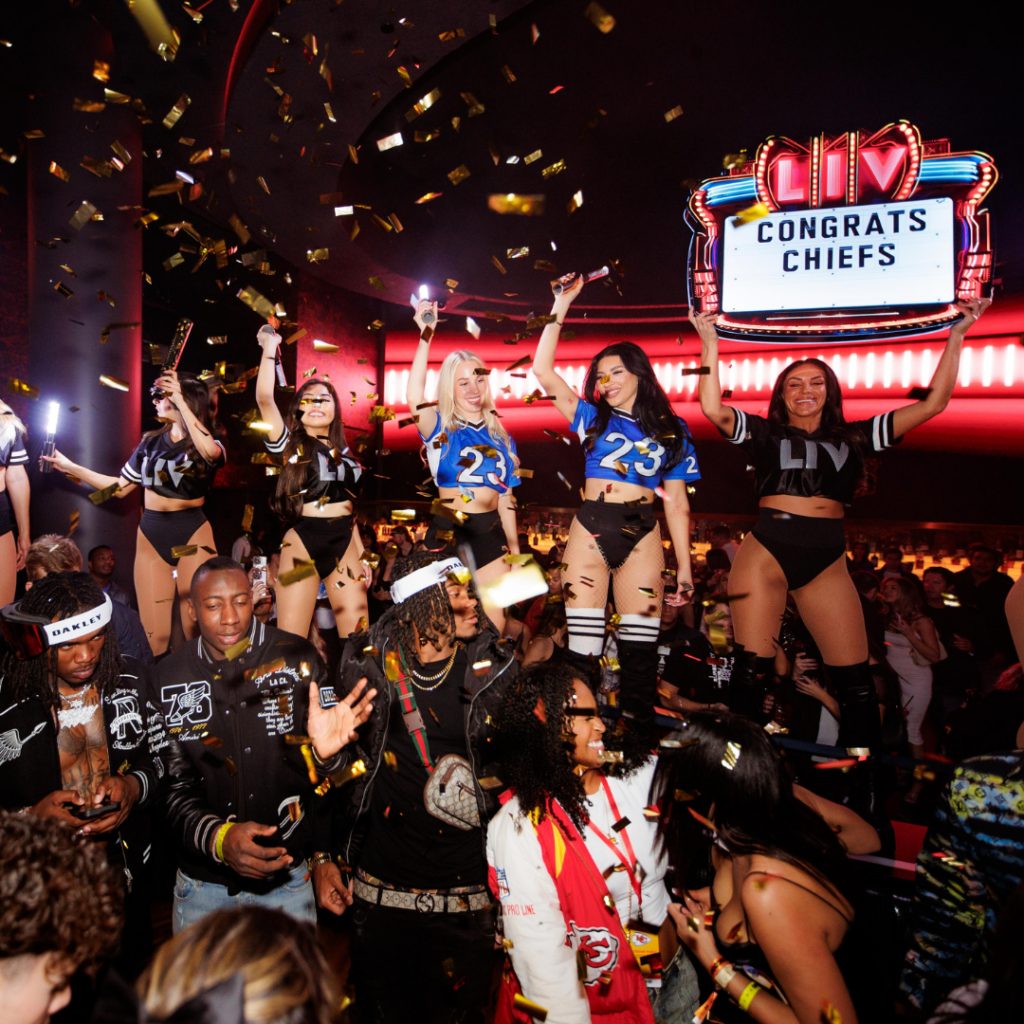 Severs holding lights on top of a booth at a table with a sign that says "CONGRATS CHIEFS" and confetti in the air